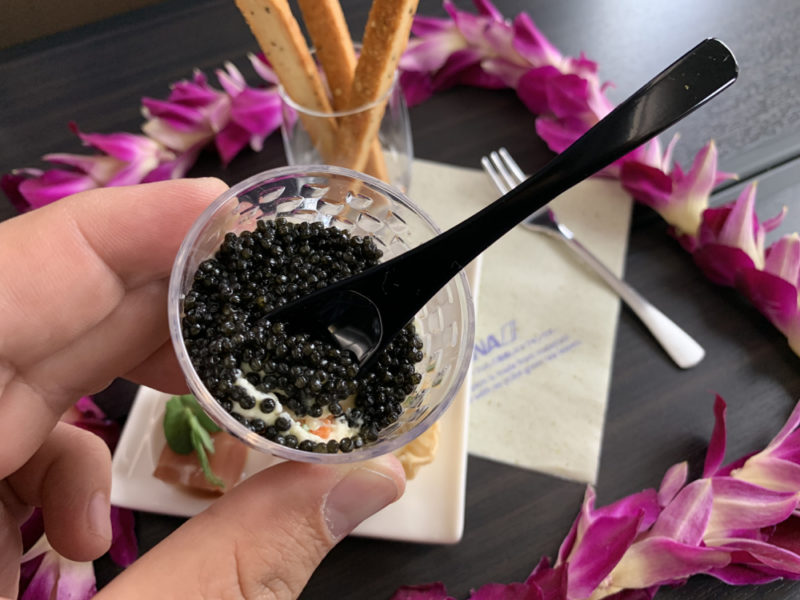 a hand holding a plastic container with black caviar