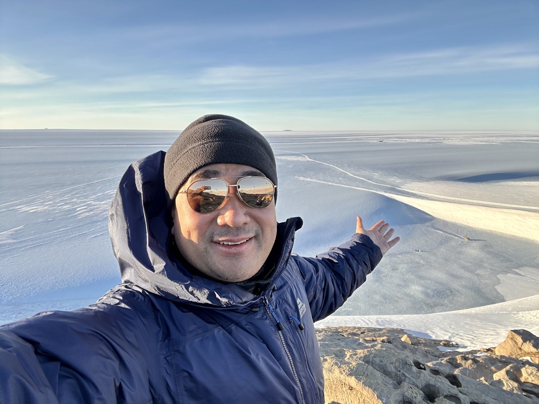 a man wearing sunglasses and a hat standing on a hill with snow