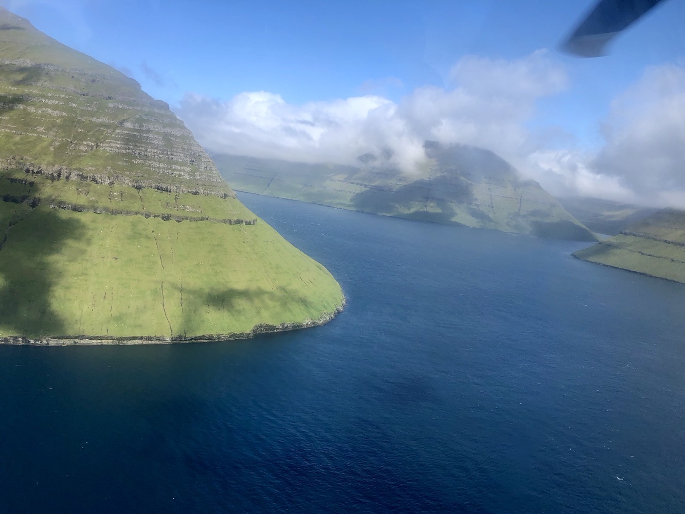 a body of water with a green hill and clouds