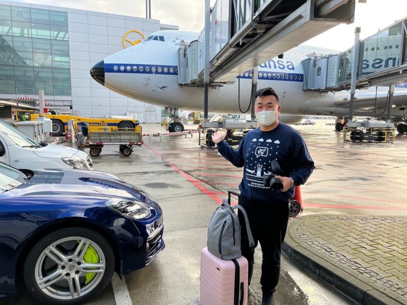 a man wearing a face mask and holding a camera and standing in front of a plane