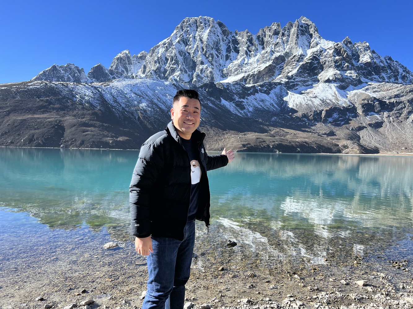 a man standing in front of a body of water with snow covered mountains in the background