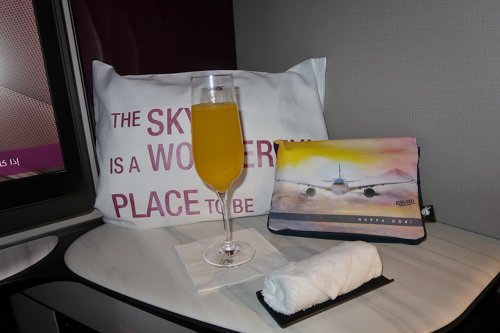 a glass of orange liquid on a table with a pillow and a towel